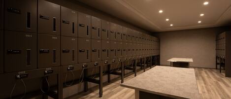 A row of metal lockers with numbers on them, a table, and a carpeted floor.