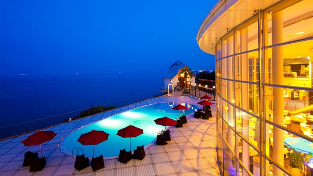 Zona de piscina con sombrillas rojas y sillones de descanso, con vistas al mar.