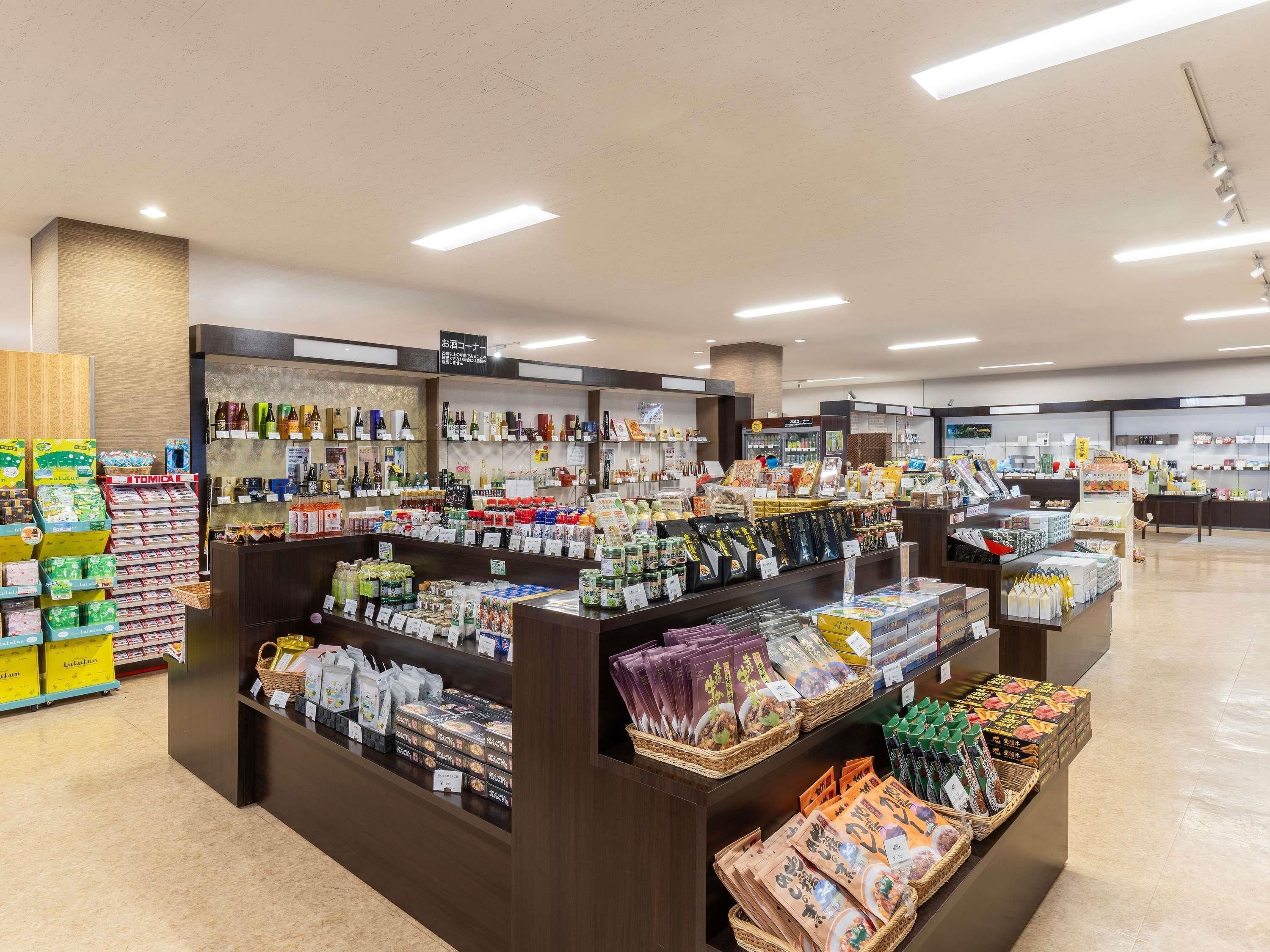Tienda bien iluminada con estantes ordenados llenos de diversos productos, incluyendo bebidas, aperitivos y alimentos envasados.