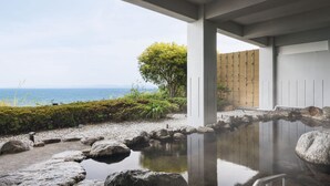 Un área de spa tranquila con un manantial termal reflectante, una valla de madera y vista al mar.