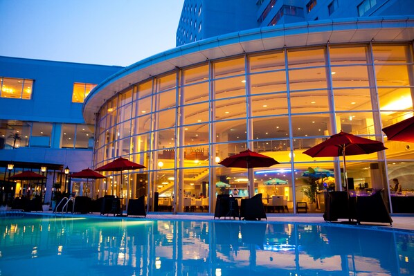 A hotel with a pool, outdoor seating, and a glass facade.