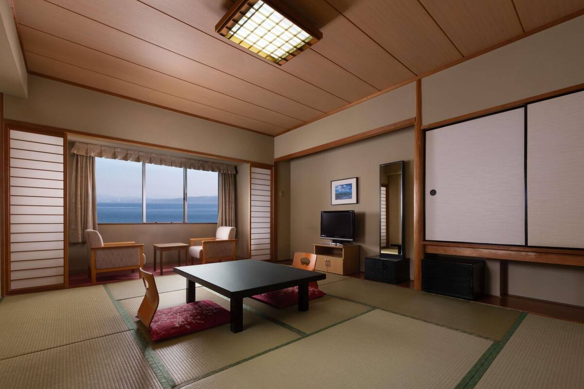 Een traditionele Japanse kamer met tatami vloerbedekking, een lage tafel, stoelen, een televisie en een grote schuifdeur.