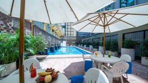 An outdoor pool area with a dining setup, including white chairs and a table with fruit and a drink. - Hotel Golden Dragon (Macau)