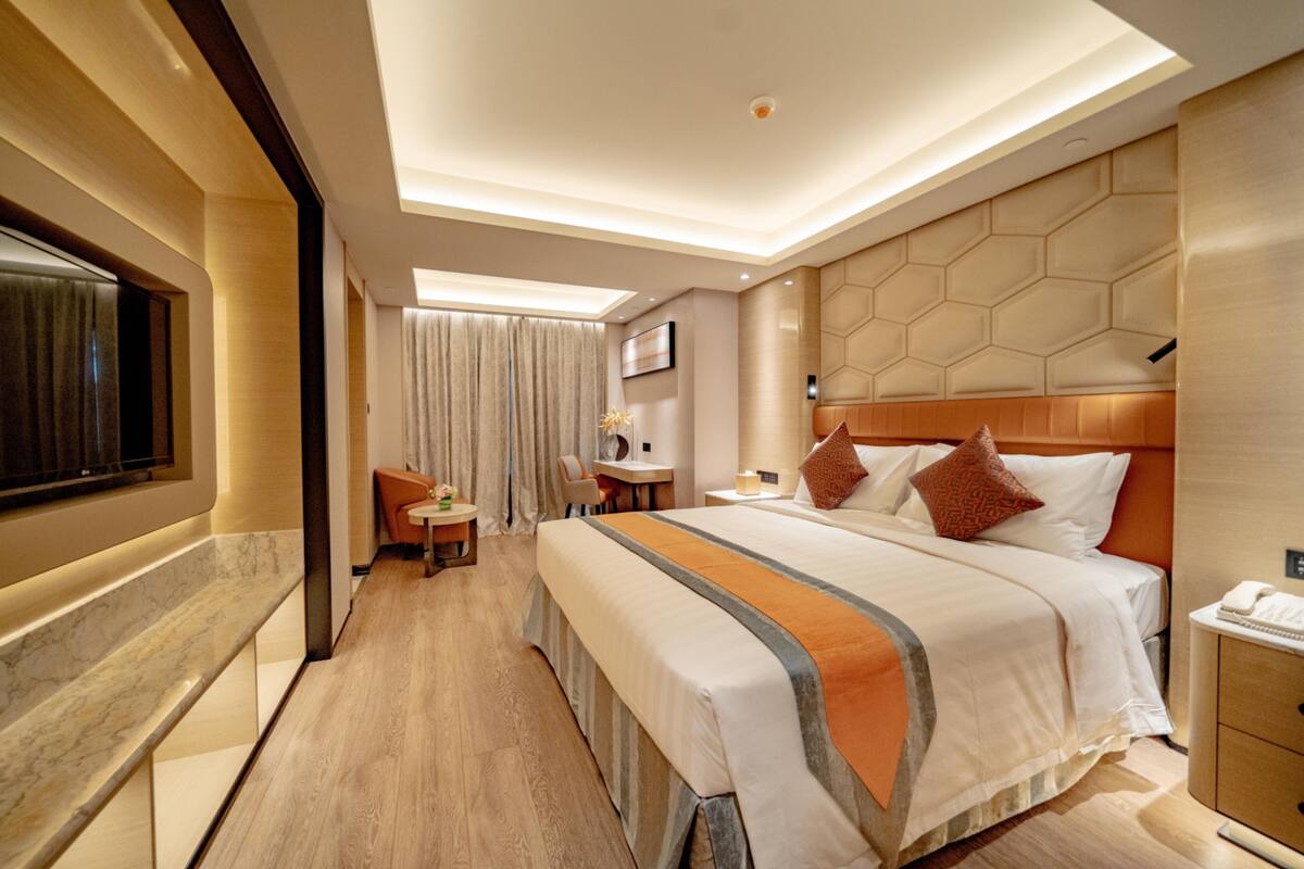 A modern hotel room with a large bed, a desk, and a seating area.