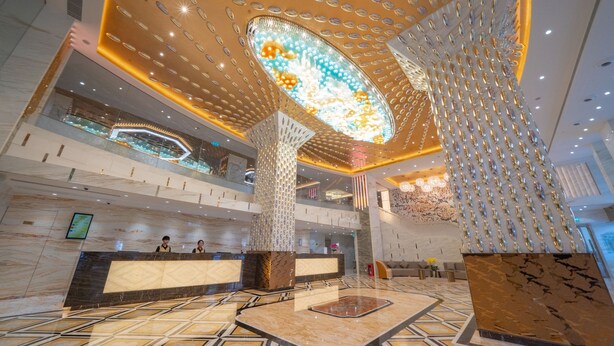 A spacious lobby with a high ceiling, a central decorative light fixture, and a reception desk. - Hotel Golden Dragon (Macau)