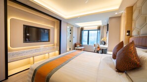 A modern hotel room with a large bed, a flat-screen TV mounted on the wall, a desk with a chair, and a city view through the window. - Hotel Golden Dragon (Macau)
