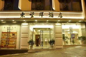 L’entrée d’un hôtel, avec une enseigne au-dessus de la porte, des plantes en pot de chaque côté et une façade en verre.