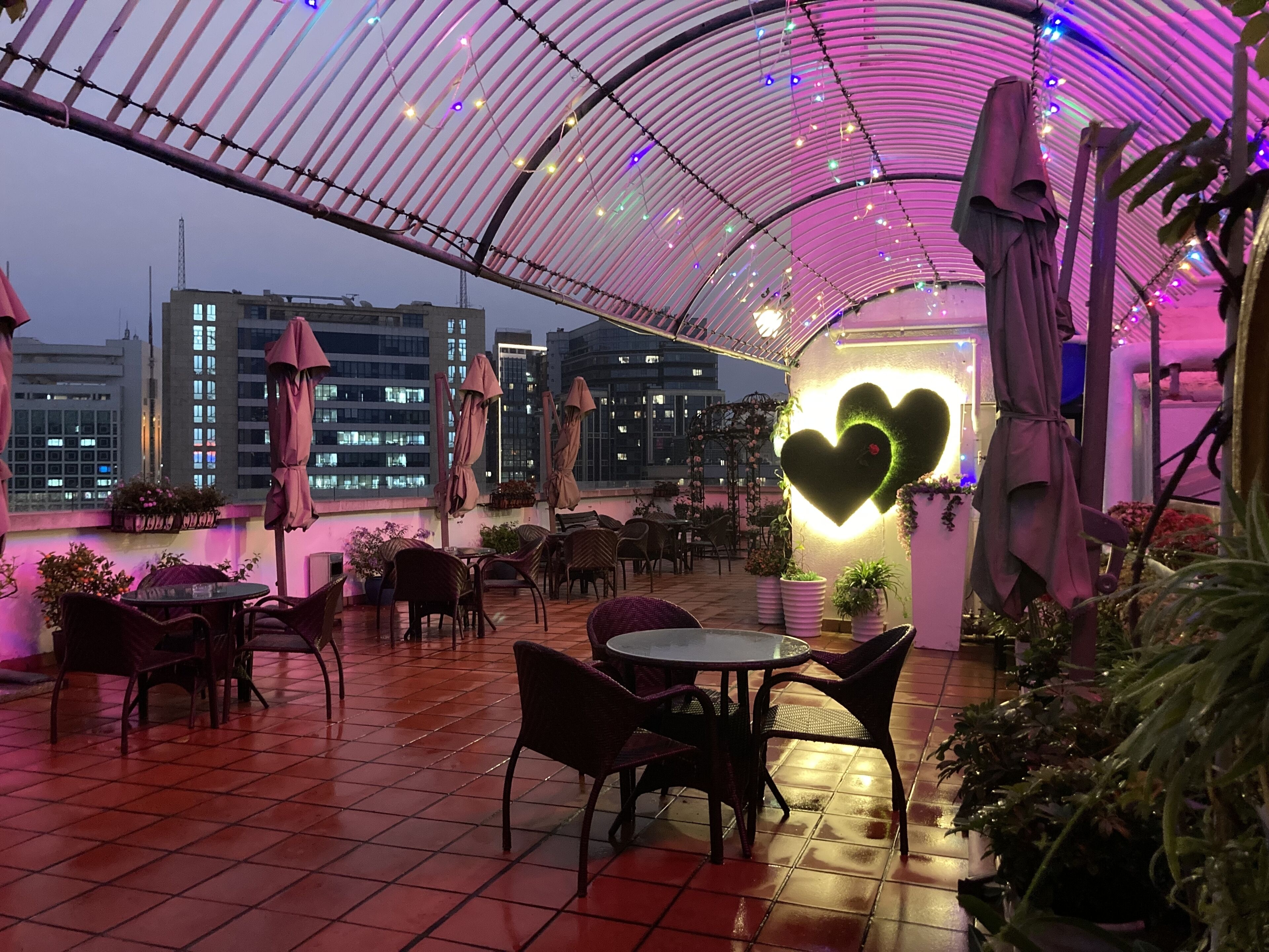 An indoor patio area with tables and chairs, a heart-shaped light fixture, and a view of buildings in the background.