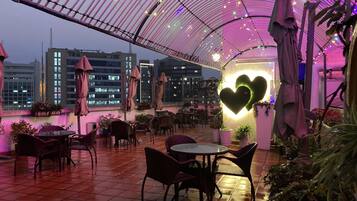 An indoor patio area with tables and chairs, a heart-shaped light fixture, and a view of buildings in the background.