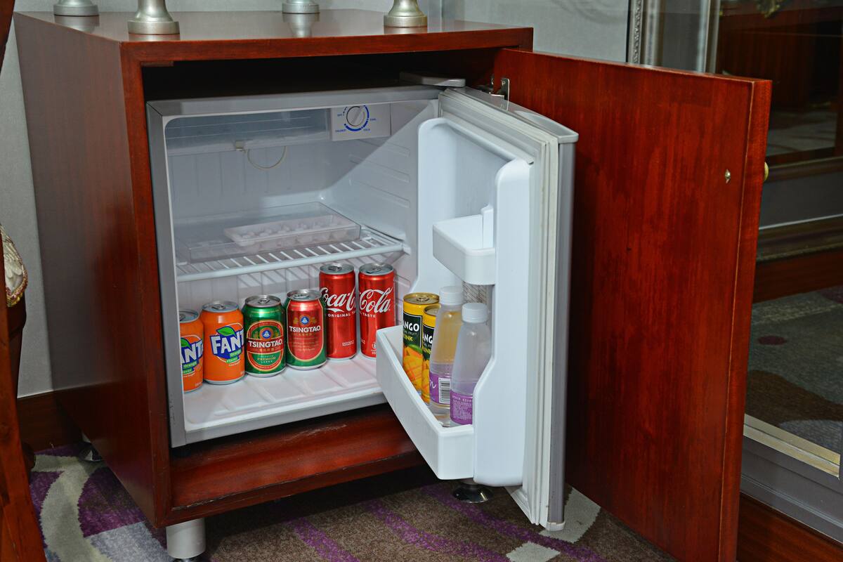 A small wooden refrigerator with a freezer compartment containing various beverages and cans.