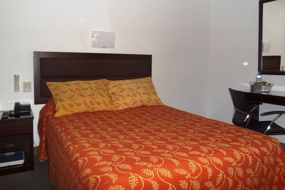 A hotel room with a bed, a desk, a chair, a telephone, and a mirror.