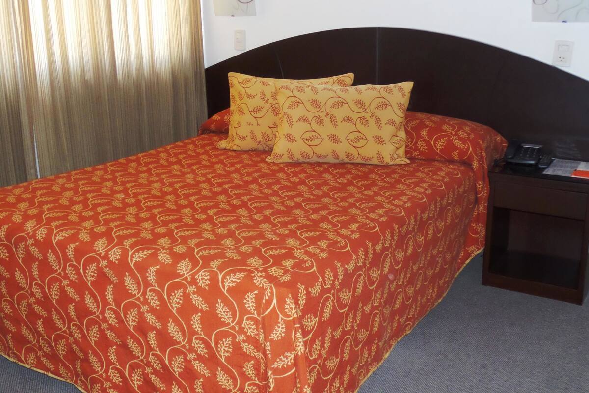A hotel room with a large bed, a nightstand, and a telephone.