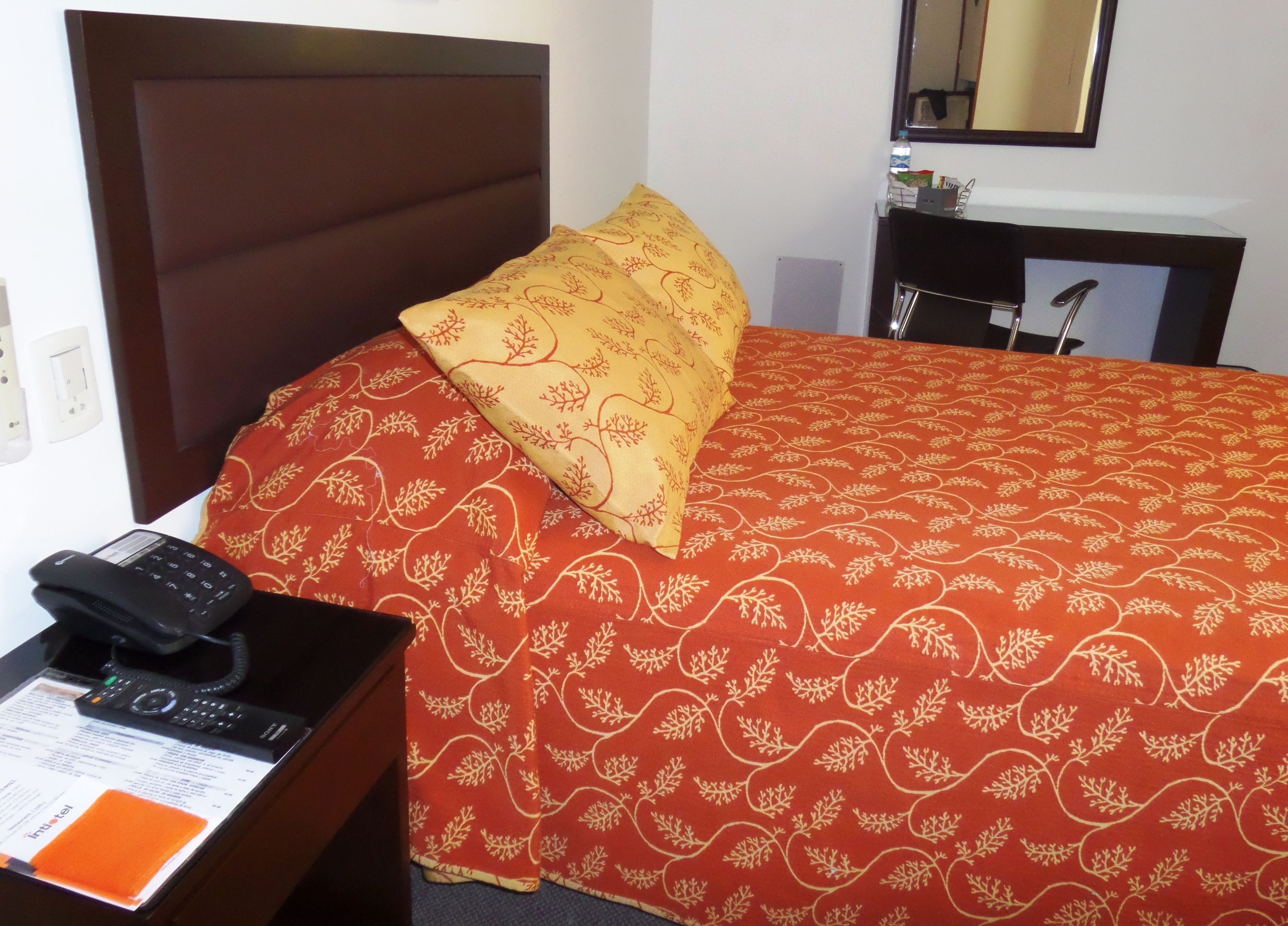 Habitación de hotel con una cama, una mesita de noche con teléfono y un escritorio con espejo y una pequeña mesa.