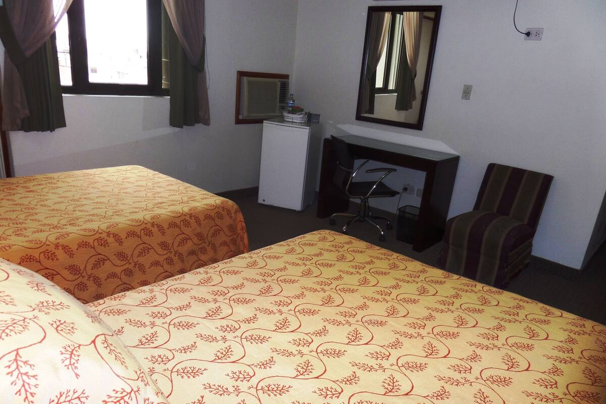 A hotel room with two beds, a desk, a chair, a mirror, and a fireplace.