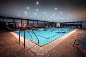 An indoor swimming pool with clear water, surrounded by lounge chairs and a tiled floor. - Hotel Haliaetum San Simon Resort (Izola)