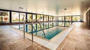 A large indoor swimming pool with clear glass walls, a tiled floor, and a metal pool ladder.