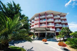 Un hotel de varios pisos con balcones, entrada cubierta y jardines tropicales.