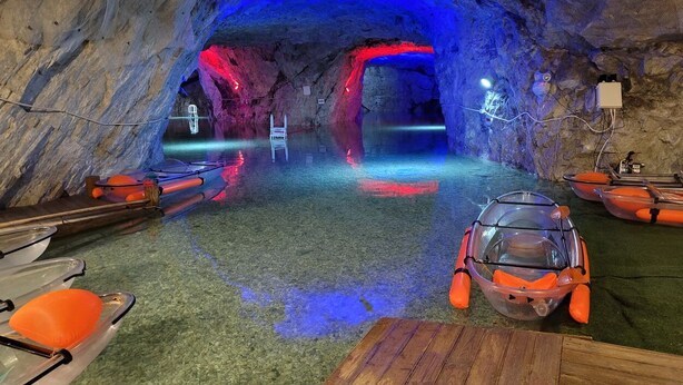 A cave-like interior with a wooden table, boats, and a glass-walled vehicle.