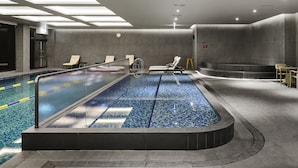 Una piscina interior moderna con separadores de carril, sillas de descanso y suelo de baldosas.