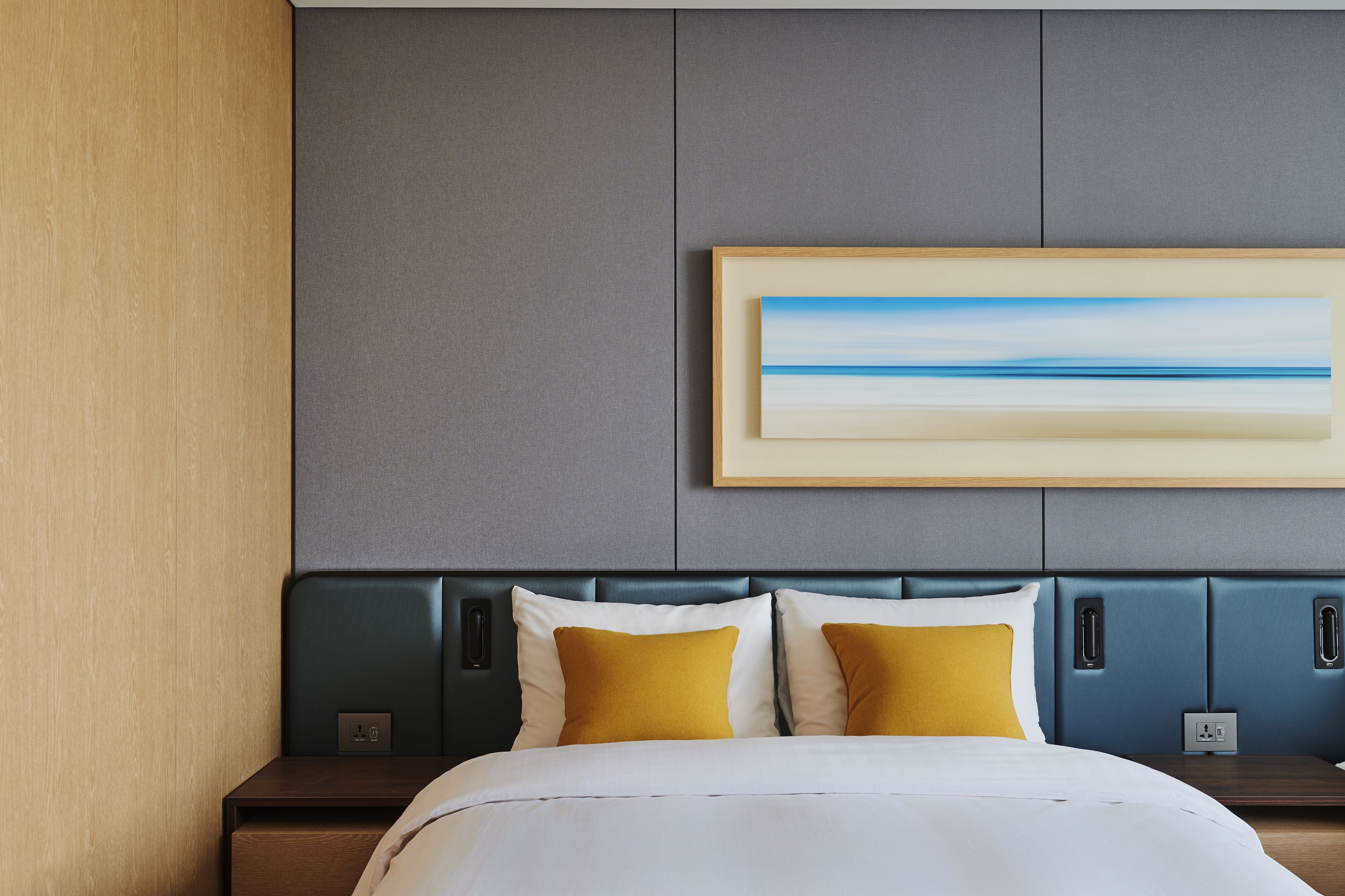 Une chambre d’hôtel avec un lit, une table de chevet, un tableau accroché au mur et une prise électrique.