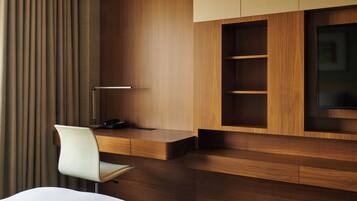 A modern hotel room with a wooden desk, a chair, a flat-screen TV, and a large window with curtains.
