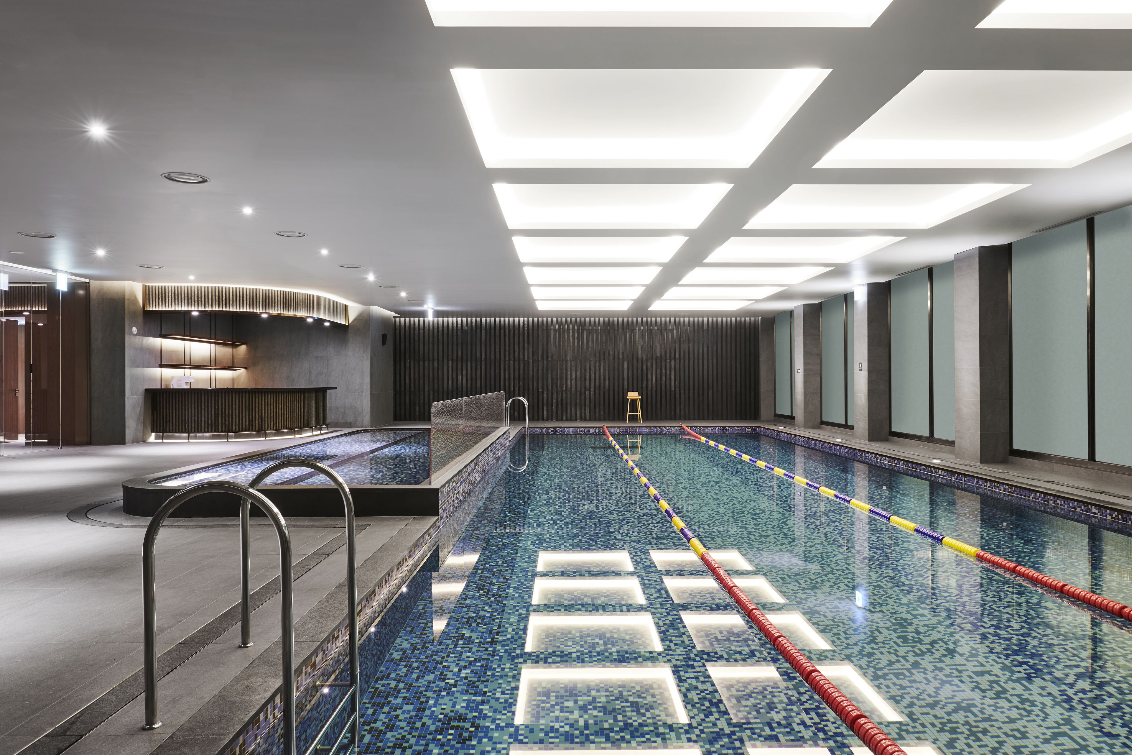 Piscina interior moderna com divisórias de pista bem definidas, um trampolim e uma área de recepção com balcão.