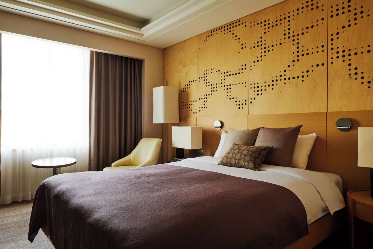 A hotel room with a large bed, a chair, two bedside tables, and a wall with a wooden panel design.