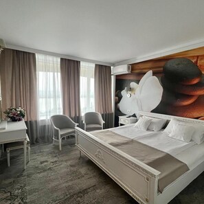 A hotel room with a large bed, two chairs, a desk, and a wall-mounted air conditioner. - Continental Drobeta Turnu Severin (Drobeta-Turnu Severin)