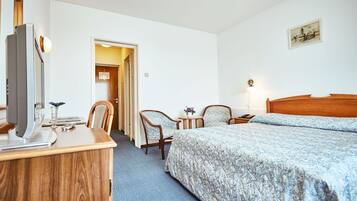 Ein Hotelzimmer mit Holztisch, zwei Stühlen, einem Bett mit floralem Bettzeug, einem Nachttisch und einer Wandlampe.
