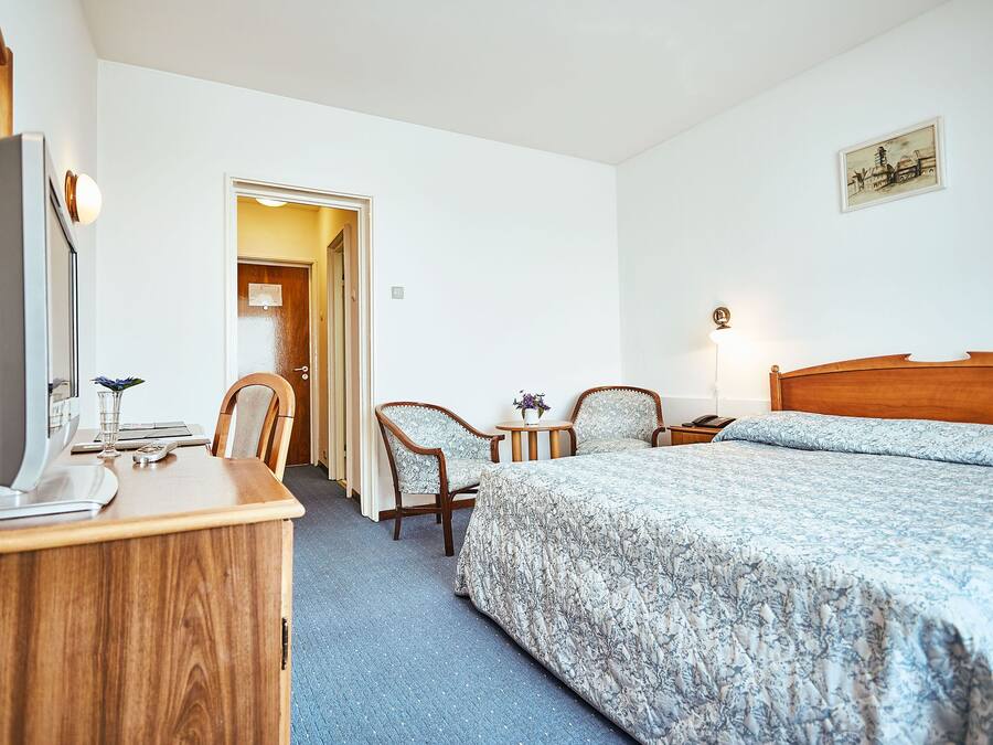 Ein Hotelzimmer mit Holztisch, zwei Stühlen, einem Bett mit floralem Bettzeug, einem Nachttisch und einer Wandlampe.