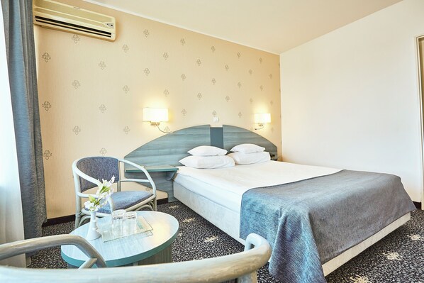 Habitación de hotel con cama, dos mesitas de noche, una silla, una mesita pequeña y un equipo de aire acondicionado.