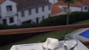 A dining table with a plate of food, a glass of red wine, and a view of a coastal town at sunset.