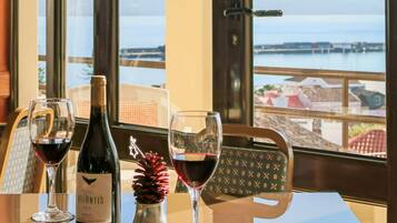 Una mesa con una botella de vino y dos copas, una piña y vistas al mar a través de amplios ventanales.