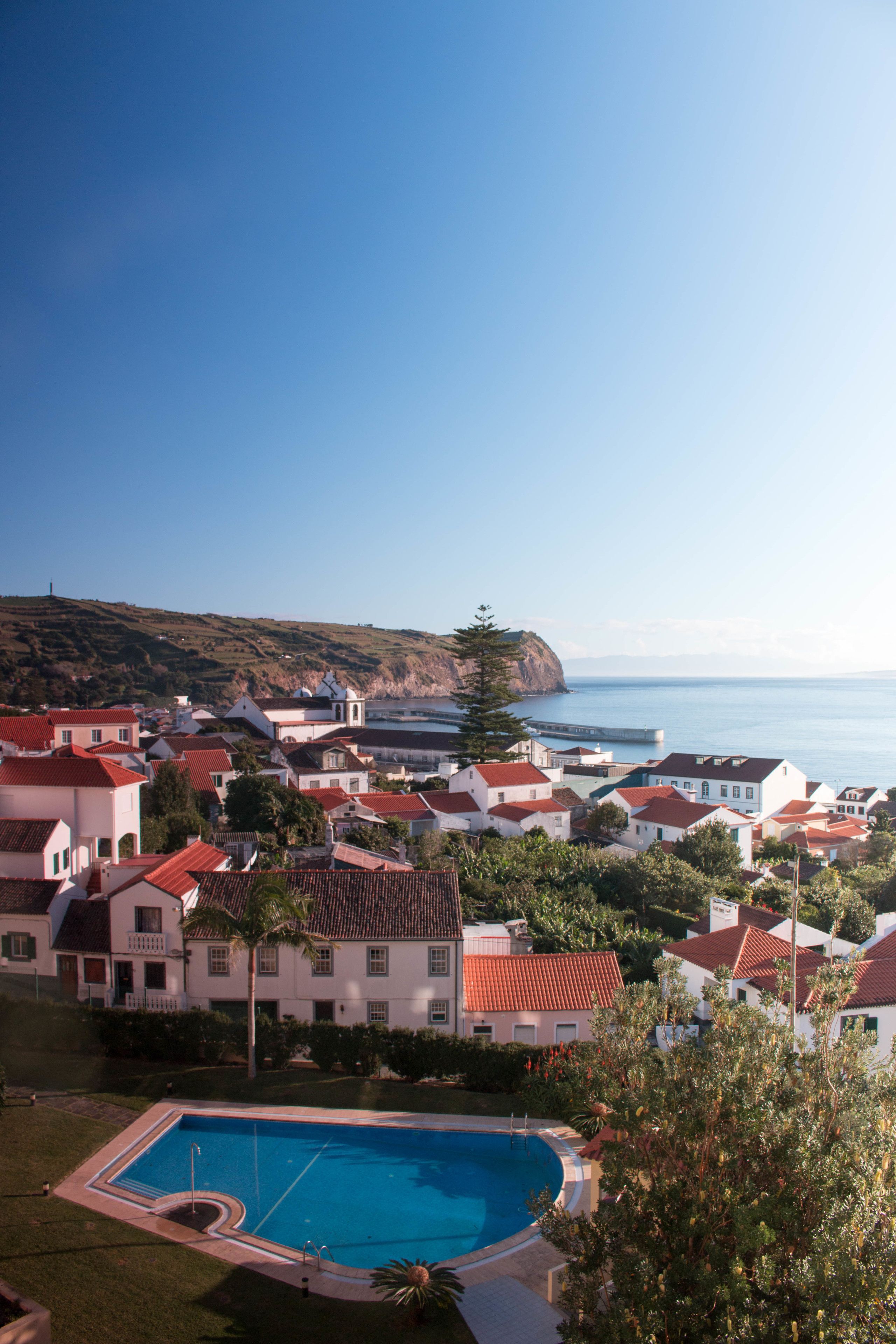 A coastal resort with a swimming pool, red-roofed buildings, and a view of the sea.