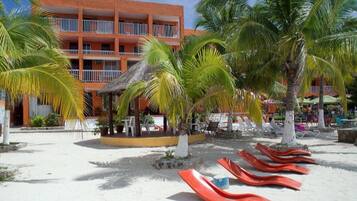 A resort with a beach area, palm trees, and a building with balconies.