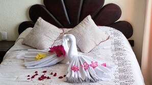 A bed with a decorative headboard, white linens, and a swan-shaped towel arrangement with flowers.