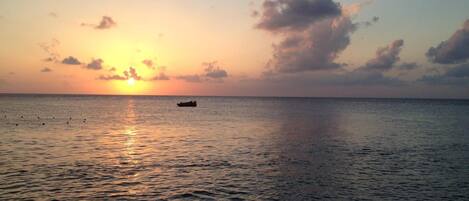 A calm sea at sunset with a boat in the distance.