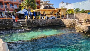 A clear waterfront area with a pool, a building with a mural, and outdoor seating.