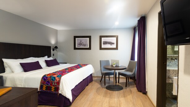 A hotel room with a bed, a desk, a chair, a small table with a laptop, and a TV. - Hotel Flamingo Inn (Querétaro)