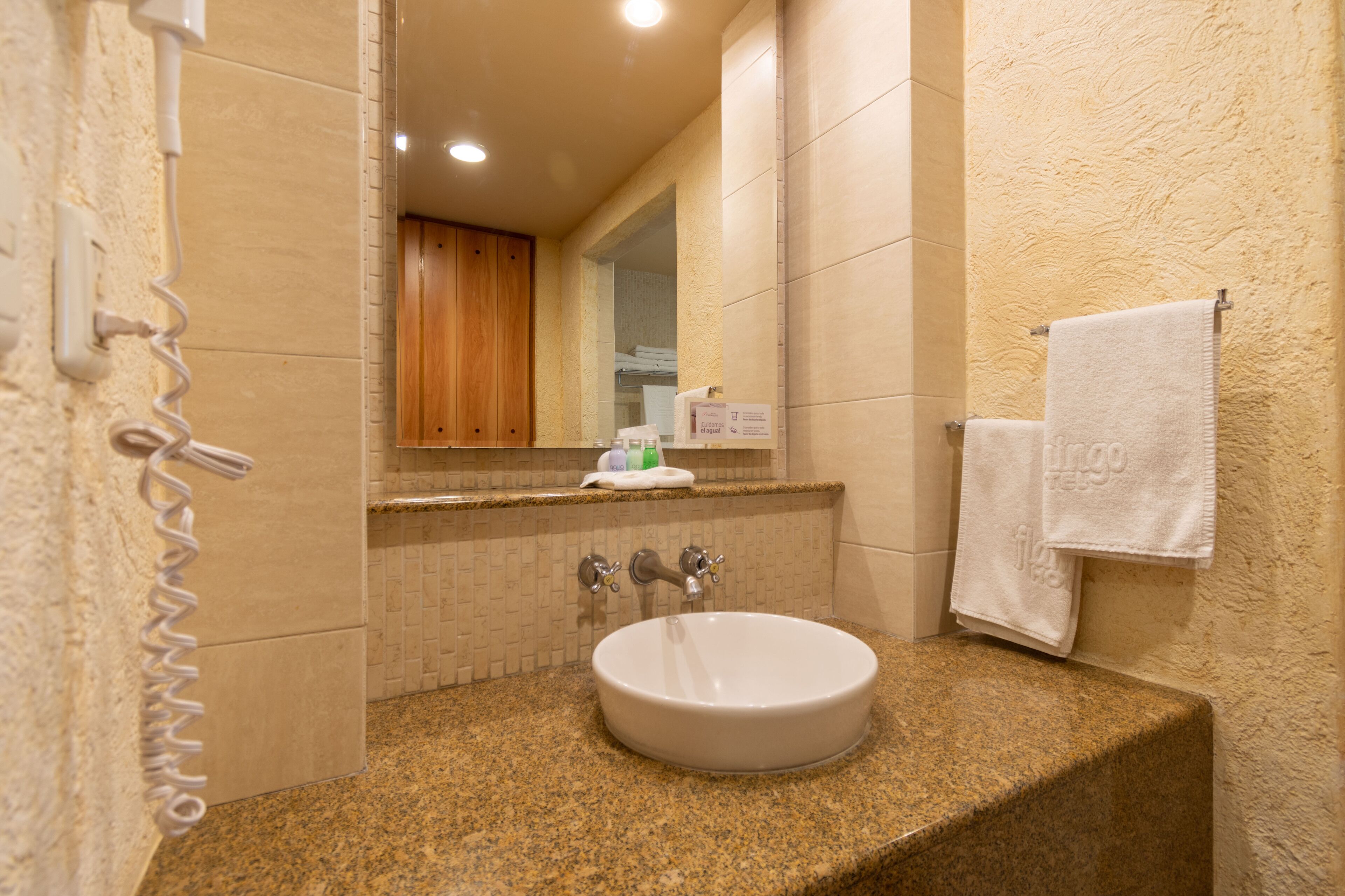 Un baño con encimera de granito, un lavamanos blanco, un espejo y un perchero para toallas.