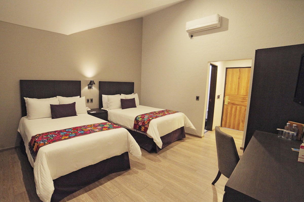 A hotel room with two beds, a desk, and a door.