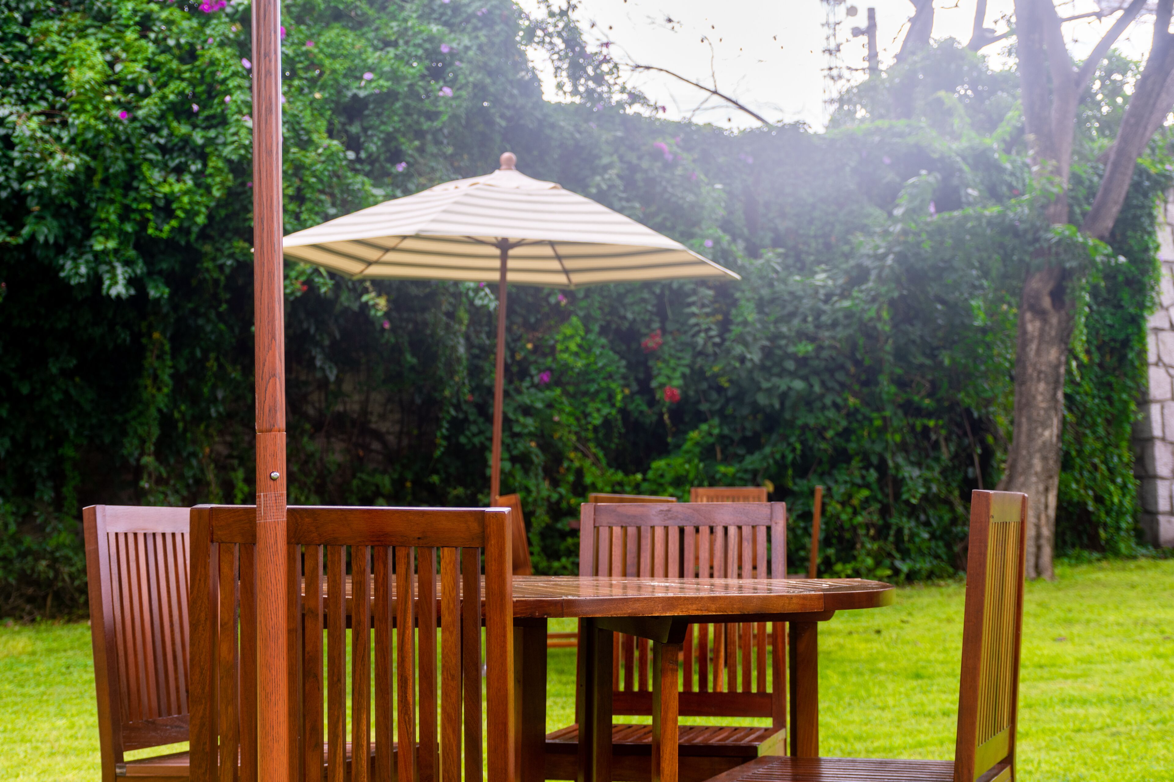 A wooden table and chairs set outdoors with a striped umbrella.