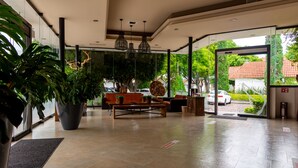 A spacious lobby with a large potted plant, a wooden bench, and a glass door leading outside. - Hotel Flamingo Inn (Querétaro)