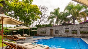 A swimming pool with lounge chairs and umbrellas, surrounded by stone walls and greenery. - Hotel Flamingo Inn (Querétaro)