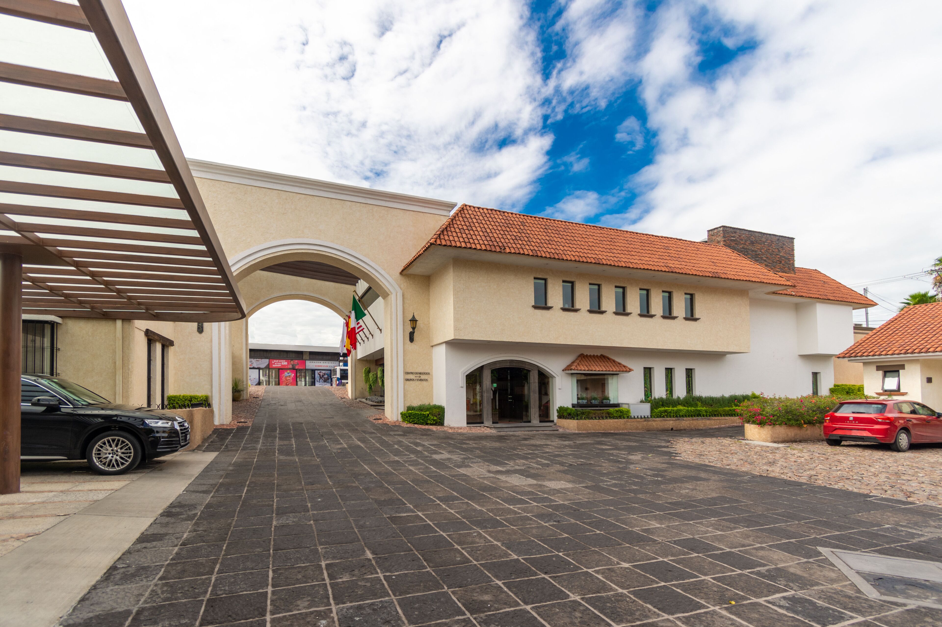 L’entrée d’un hôtel, avec une allée carrelée, un arc et une voiture rouge garée à proximité.