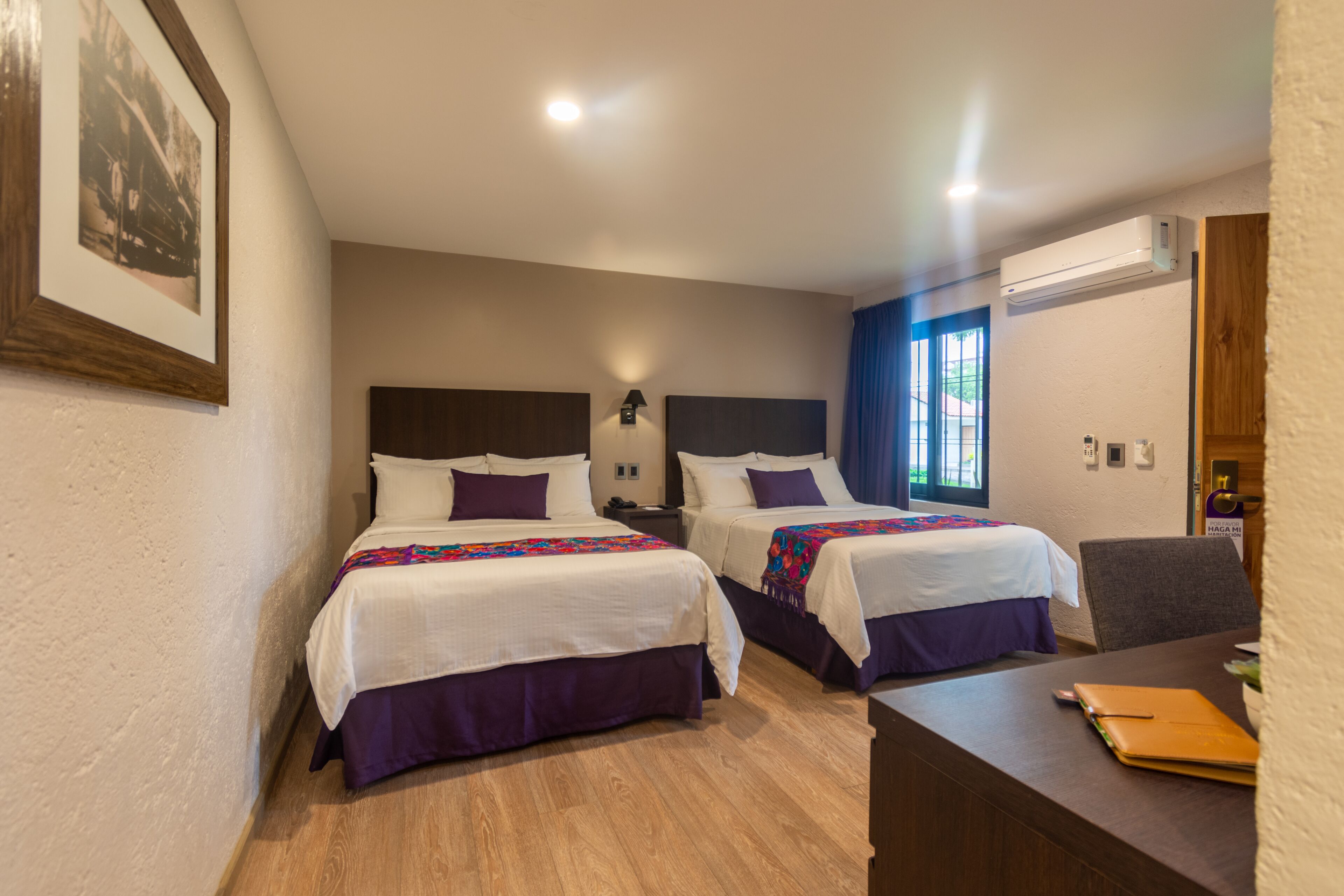 Habitación de hotel con dos camas, un escritorio y una ventana con cortinas azules.