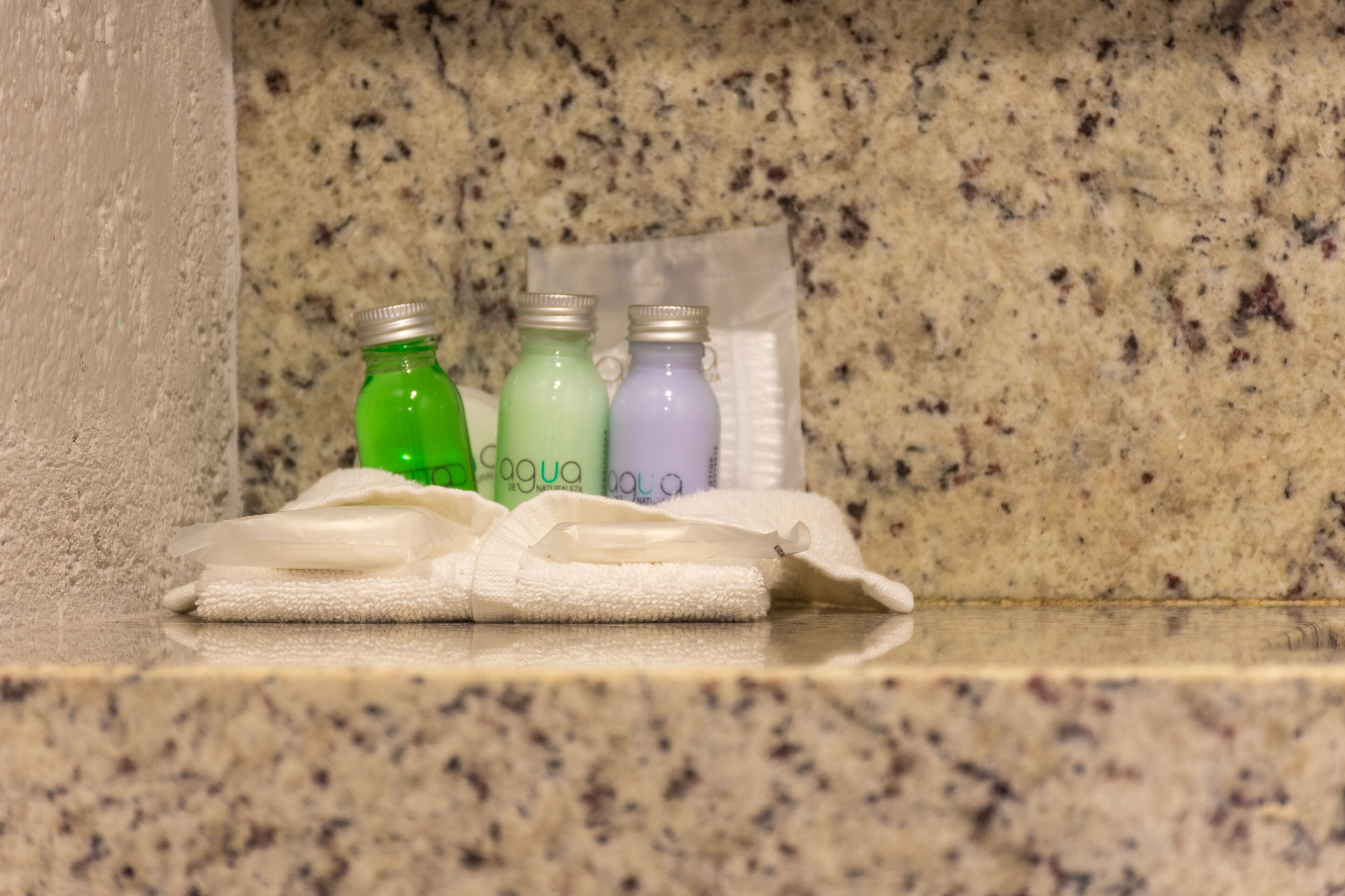 A bathroom counter with three bottles of bath products and a folded towel.