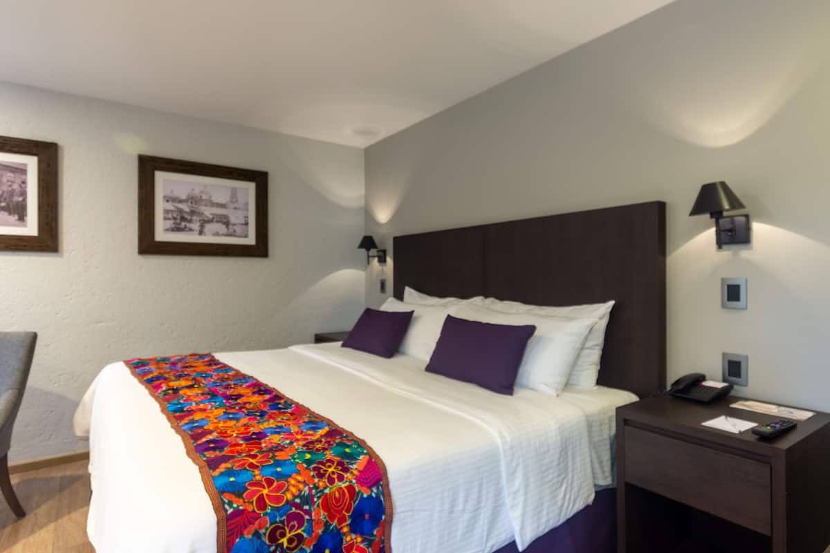A hotel room with a large bed, a nightstand with a phone, and framed pictures on the wall.
