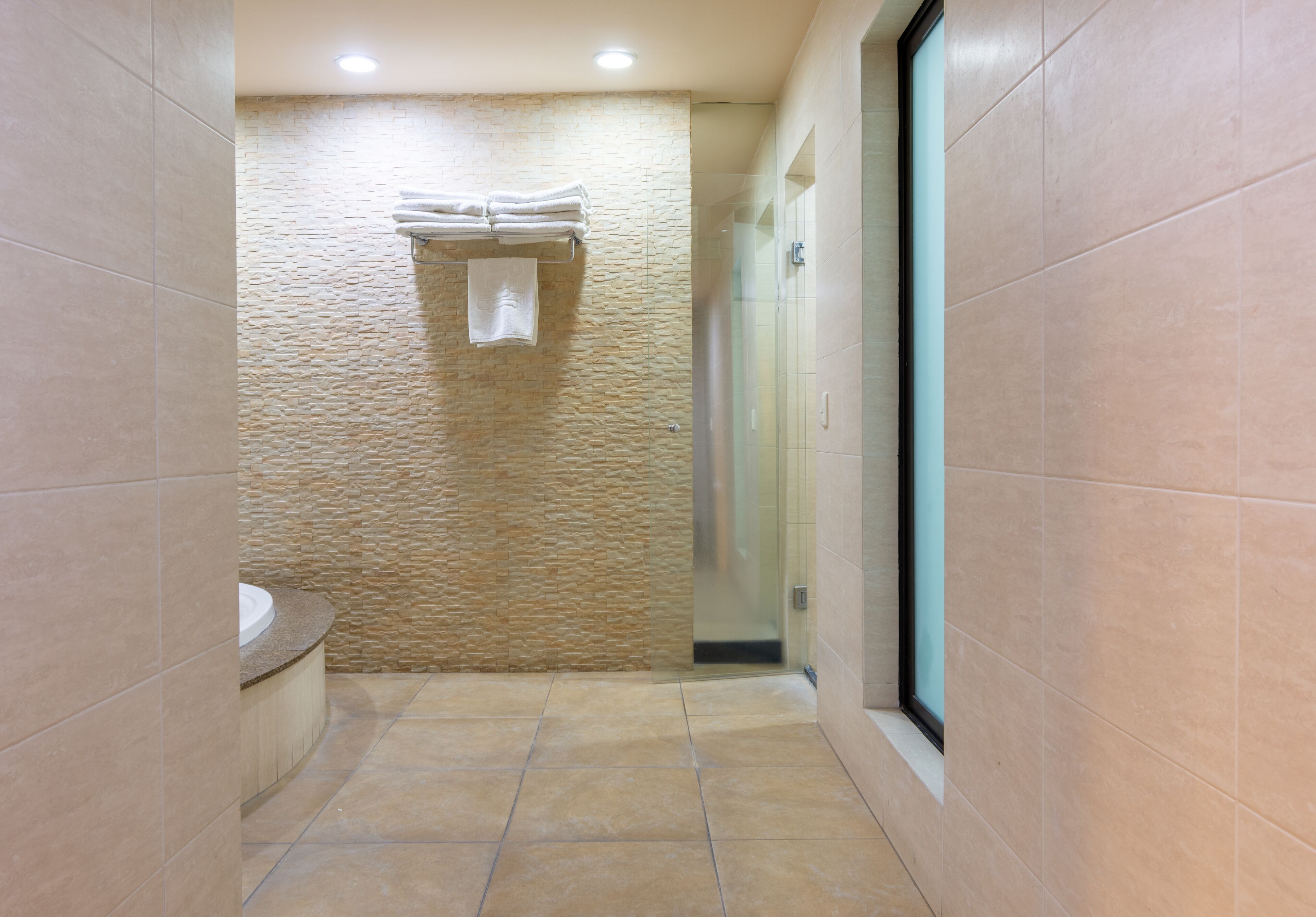 A narrow bathroom with a stone wall, a glass shower enclosure, and a sink with a beige countertop.