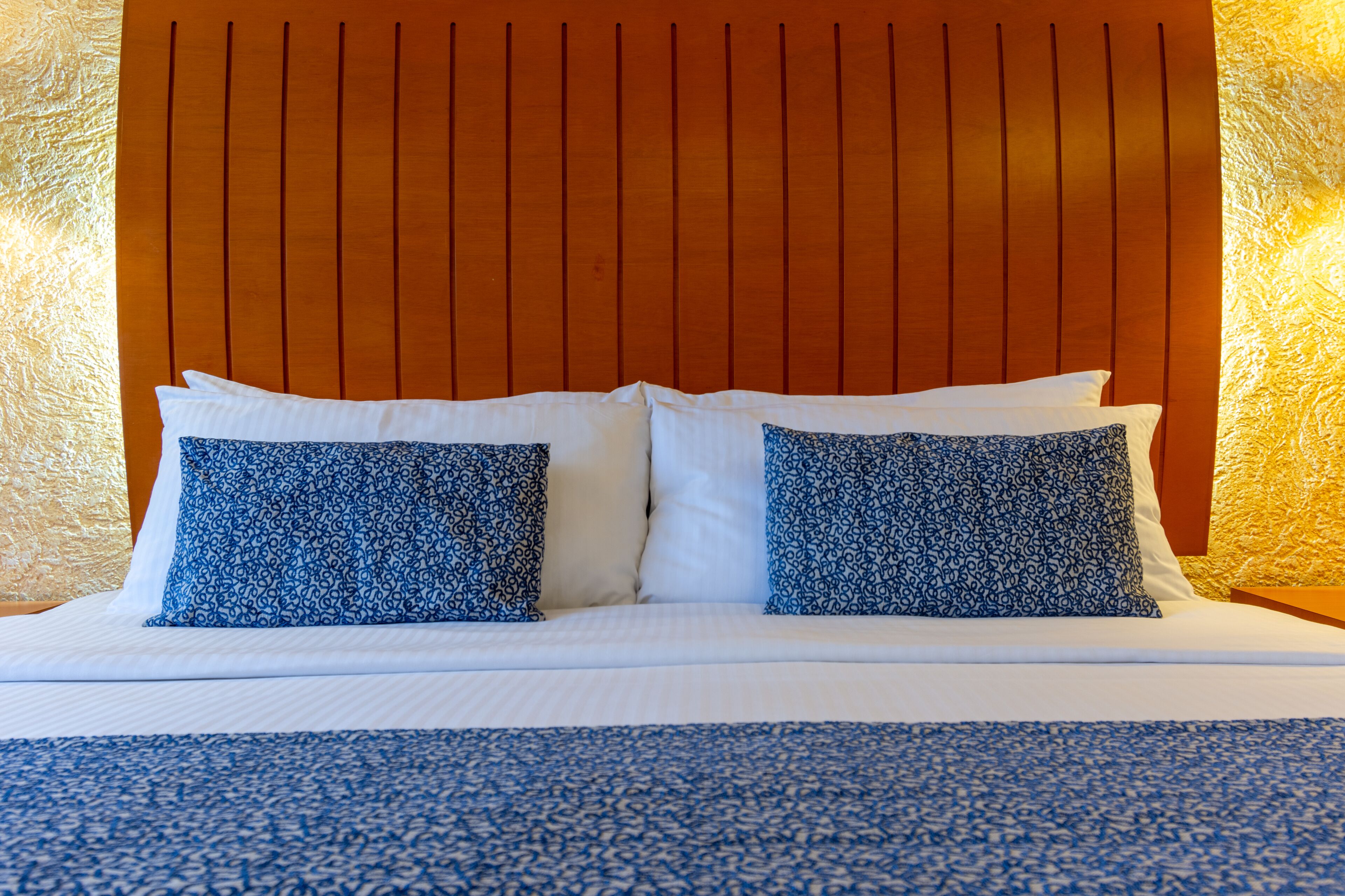 A bed with a wooden headboard, white bedding, and two patterned pillows.